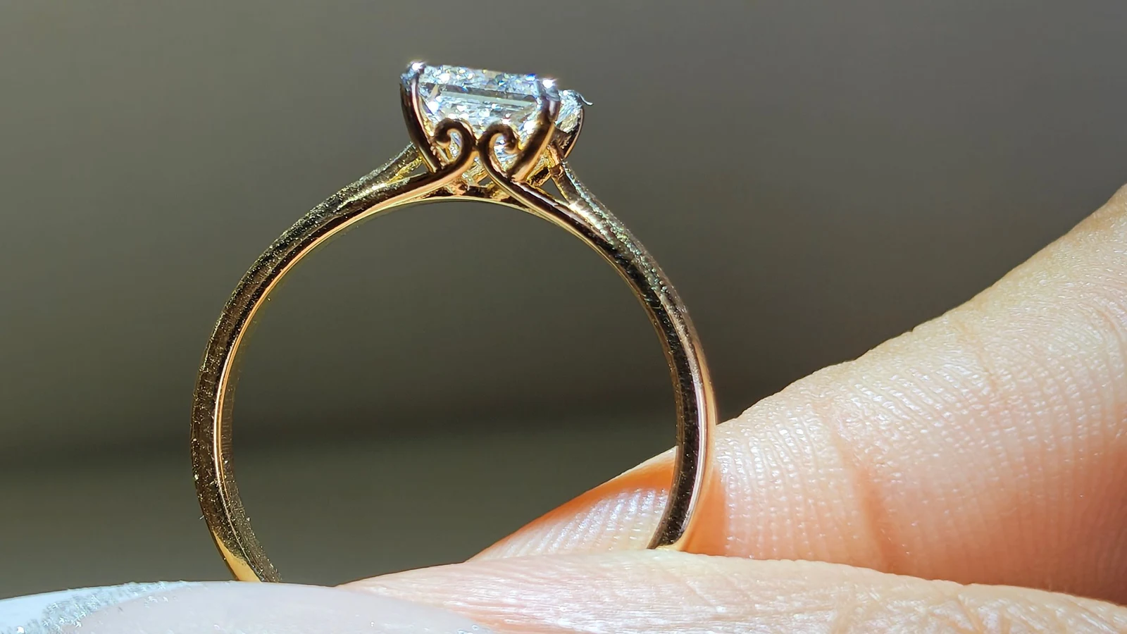 Side view of a diamond solitaire in a yellow gold setting, balanced on a fingertip