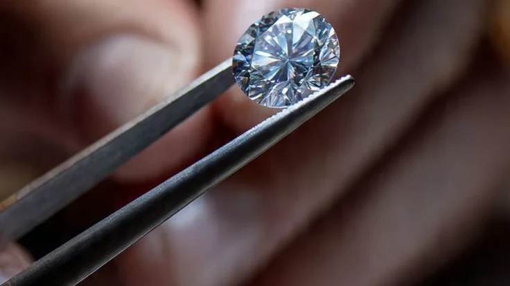 A loose polished diamond held in tweezers against a softly blurred background