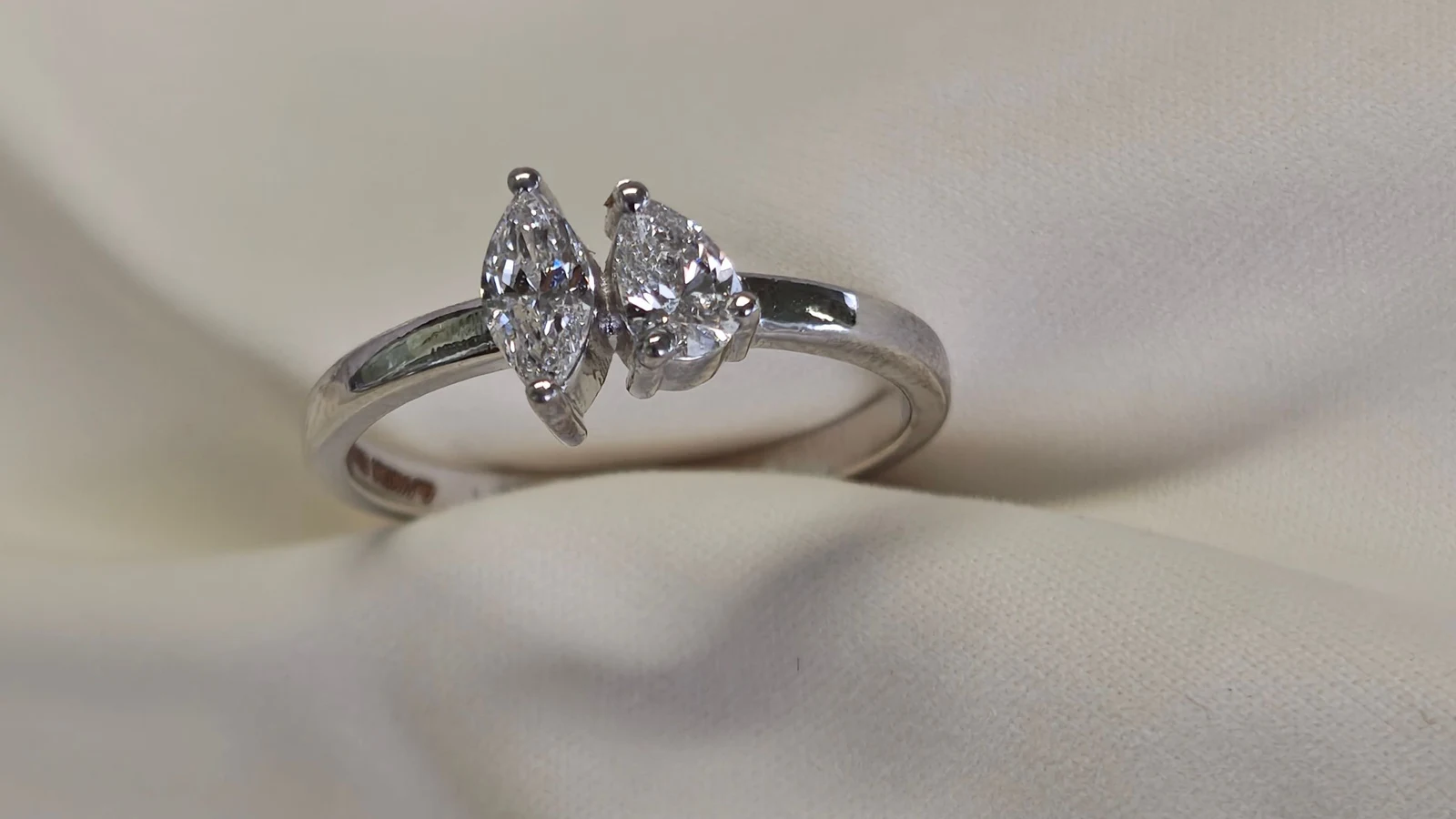 A two-stone ring with a marquise diamond and a pear-shaped diamond on cream fabric