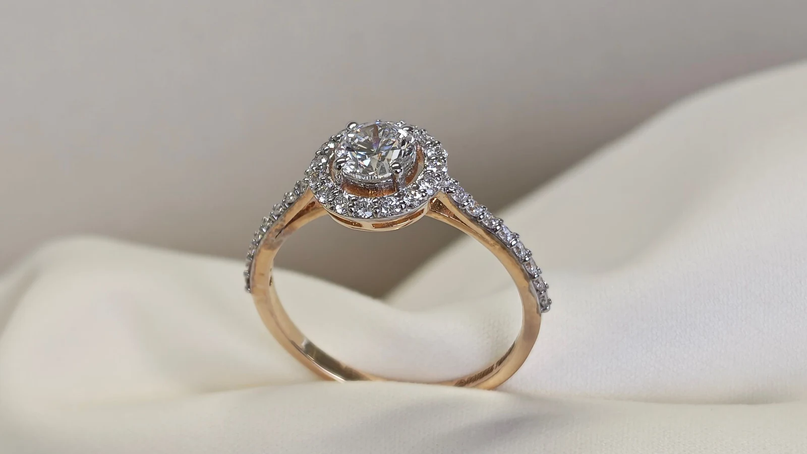 A round diamond halo ring in yellow gold resting on folded cream fabric