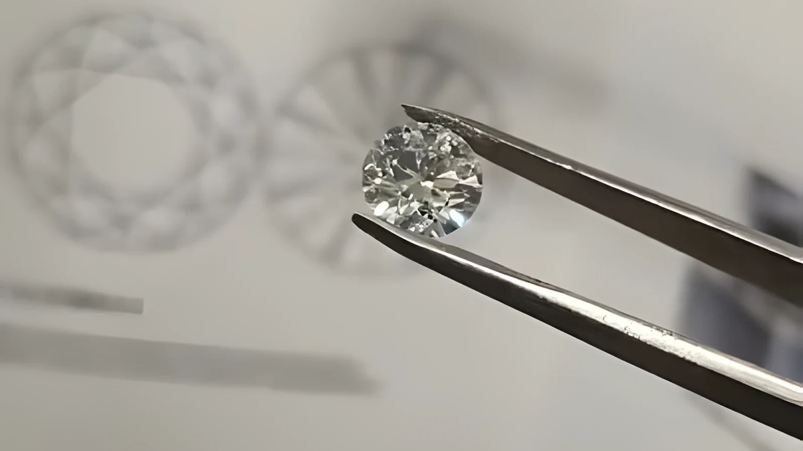 A polished round lab-grown diamond held in tweezers in front of facet diagrams